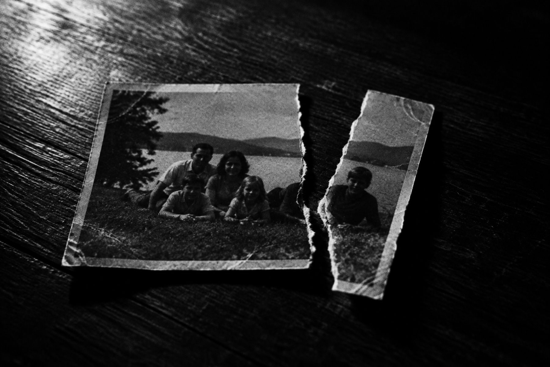 Black and white photo: a family photograph torn apart, one person ripped out