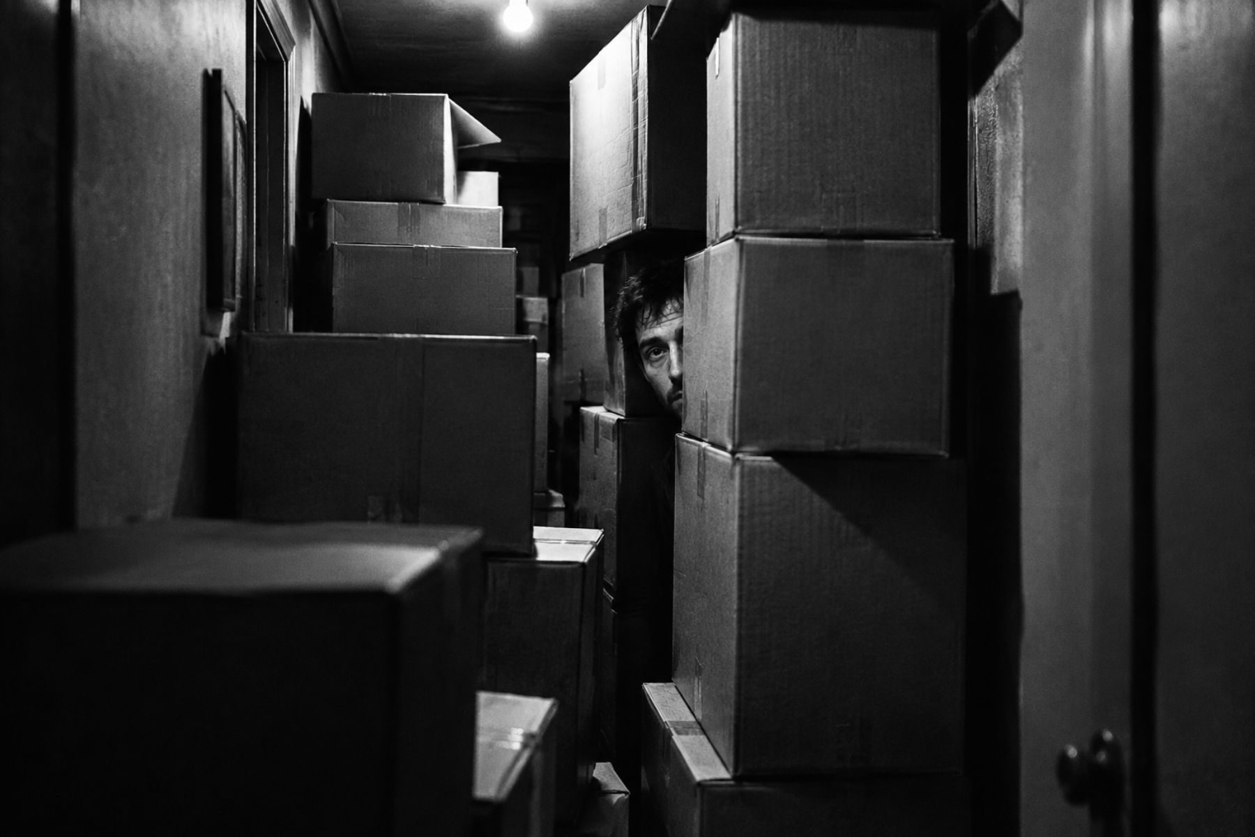 Black and white photo: a man walled in by stacked delivery boxes