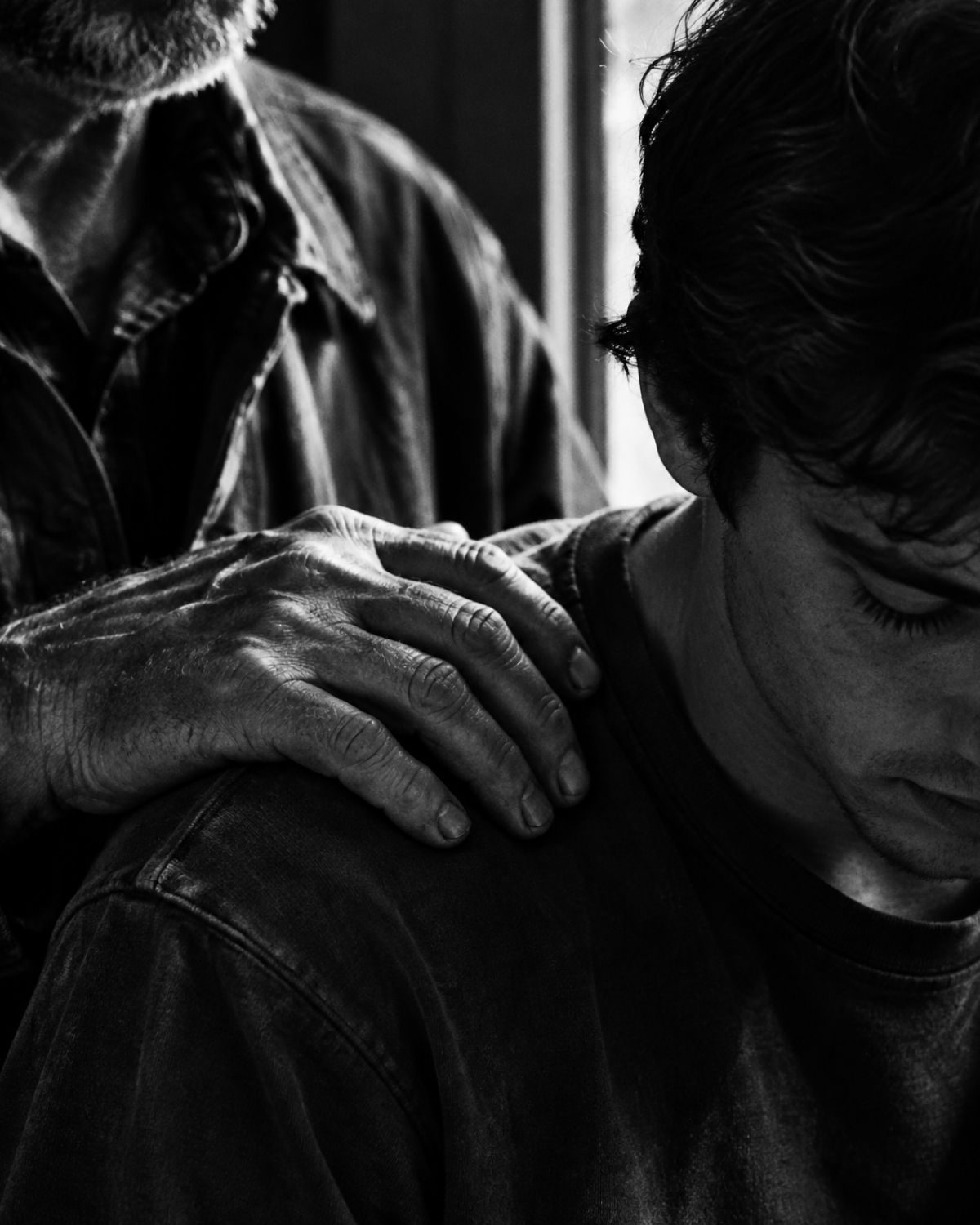 Black and white photo: an older man's weathered hand on a young man's shoulder