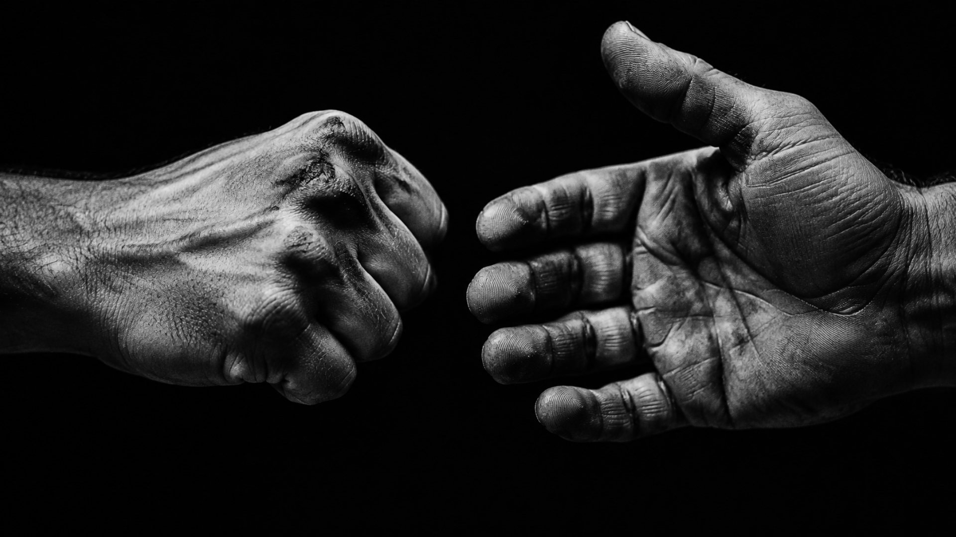 Black and white photo: a clenched fist and an open hand about to meet